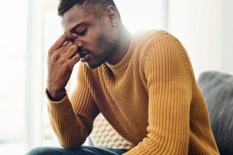 A man on a couch with his head in his hands, expressing feelings of frustration or sadness